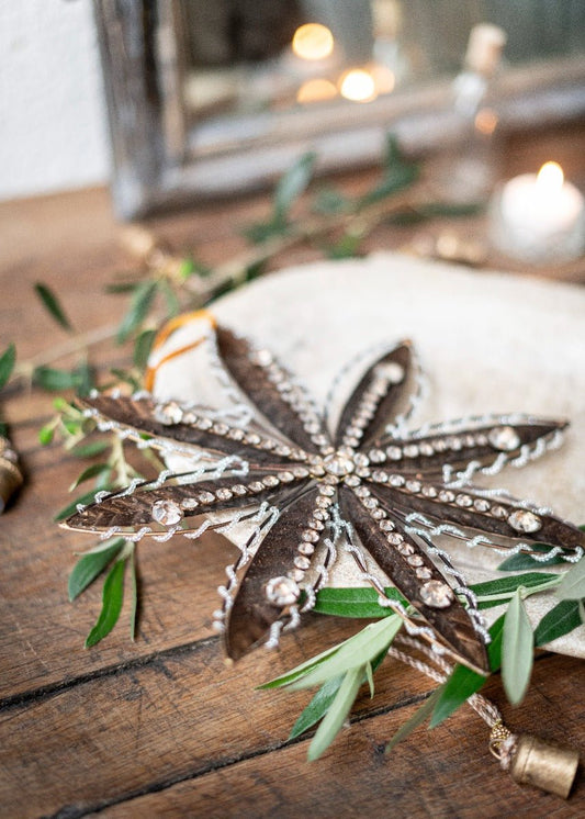Decorative star-shaped object with embellishments on a wooden surface with greenery