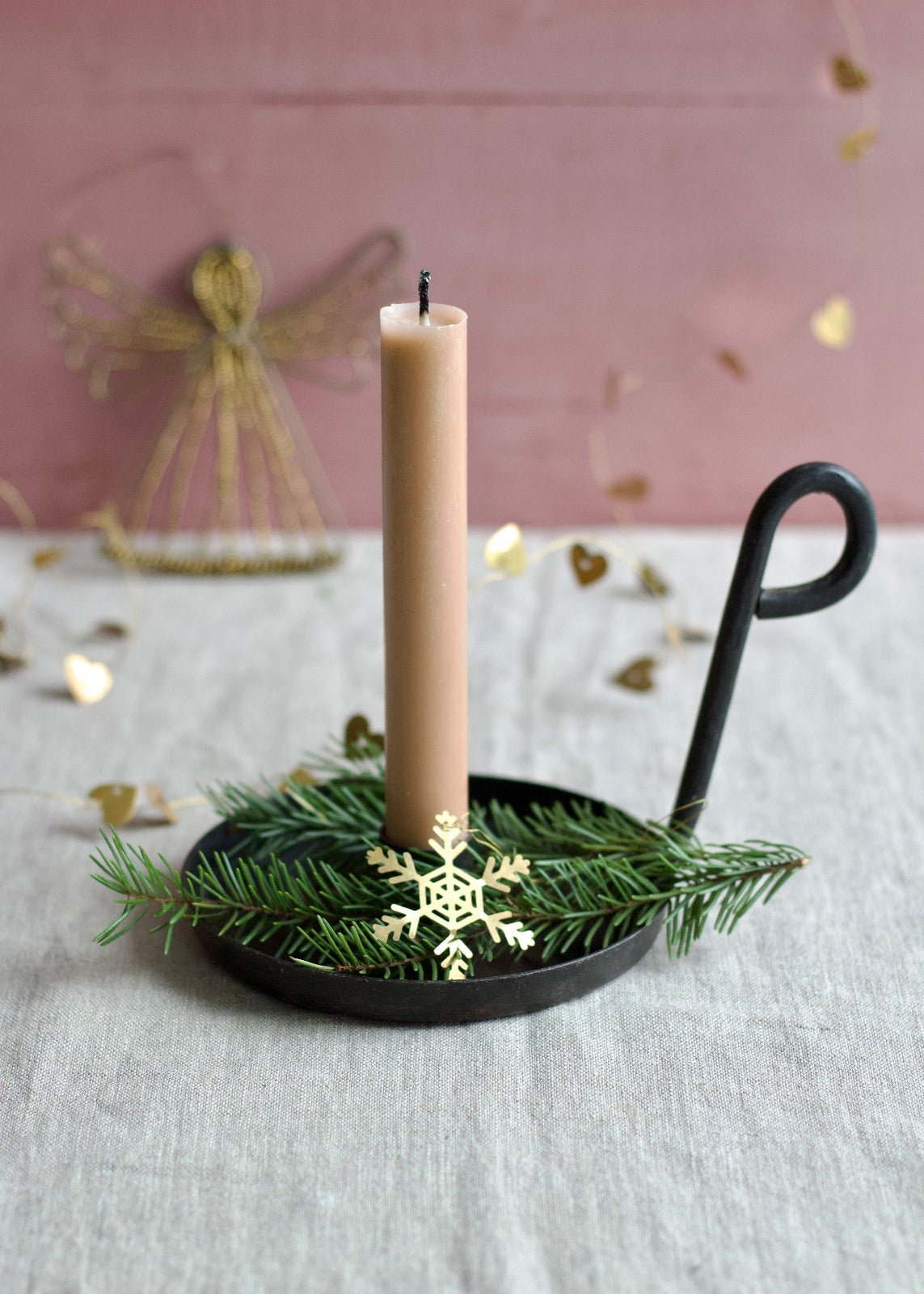 Golden brass snowflake ornament placed on fir branches in a candle holder.