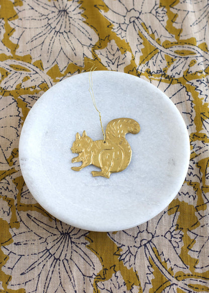 Gold squirrel pendant on a white marble coaster with a floral patterned fabric background