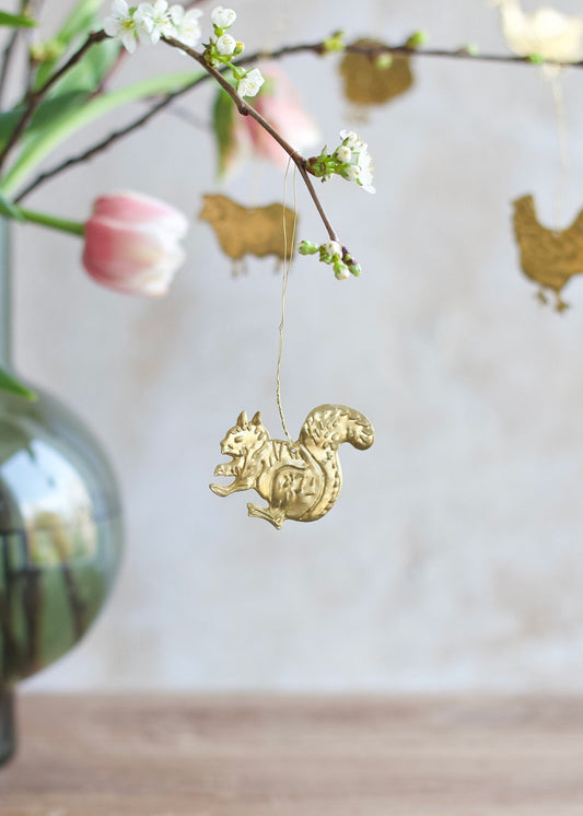 Gold squirrel ornament hanging from a branch with flowers and a blurred background