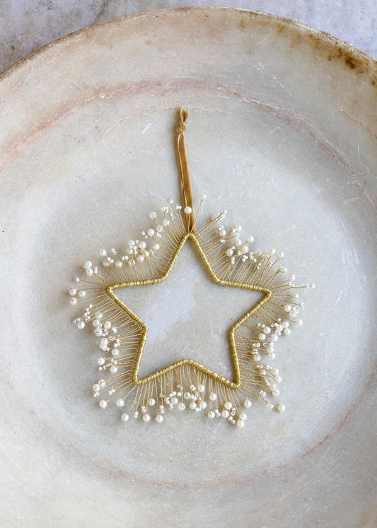 Gold-colored star adorned with white pearls, suspended on a soft velvet cord.