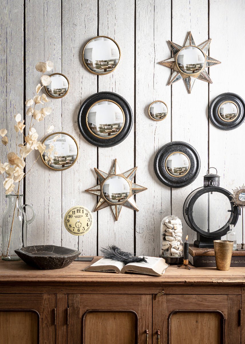 Decorative oval, start shape wall mirror with black & gold frame on a white wooden background 