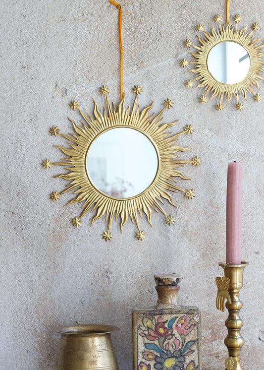 Decorative gold sunburst mirrors on a textured wall with a pink candle and decorative items.