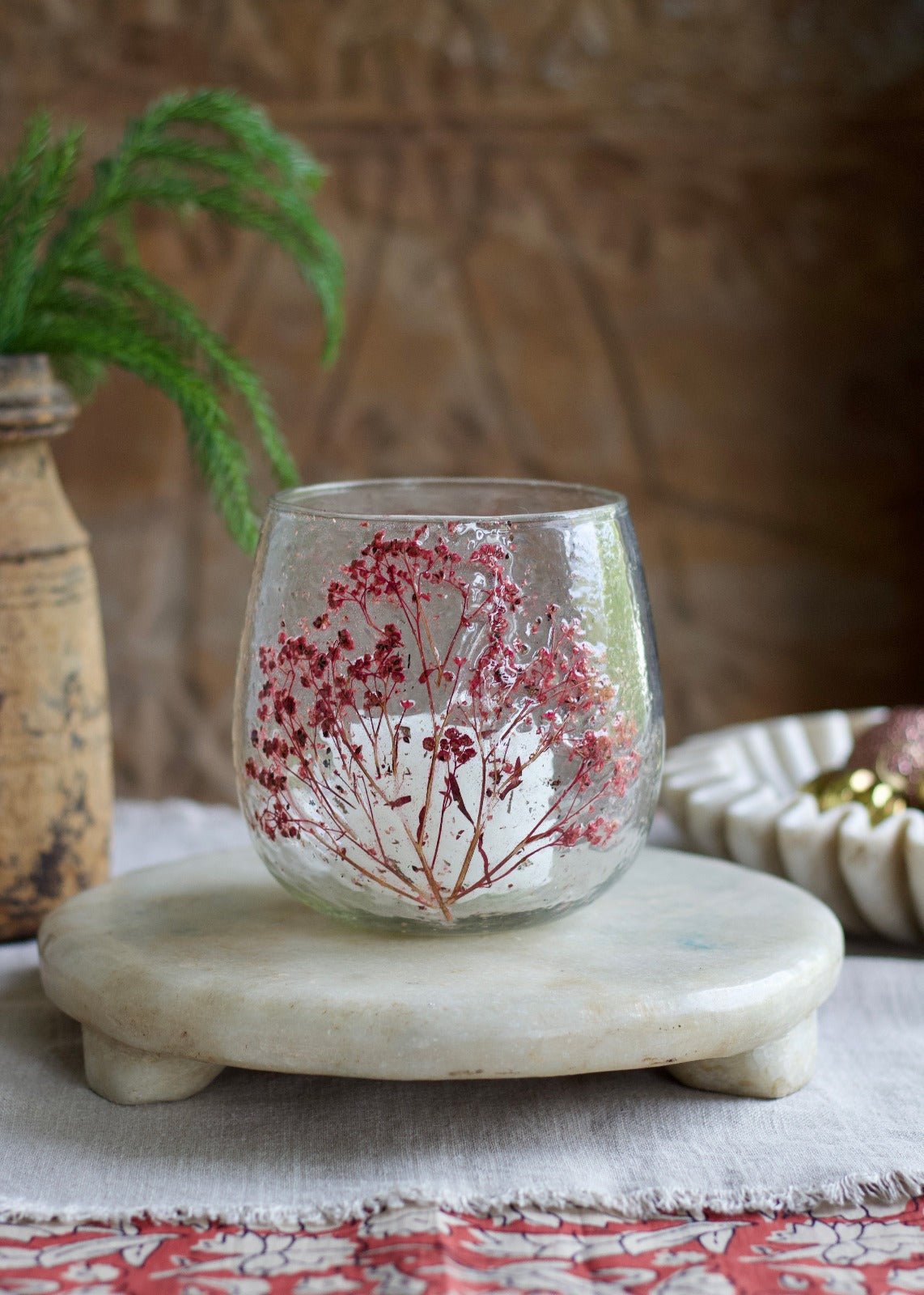 Round handmade glass tealight holder with embedded dried red flowers, placed on a light stone tray.