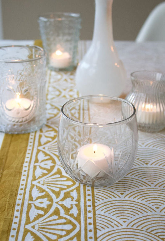 Decorative table setting with glass candle holders and a patterned tablecloth.