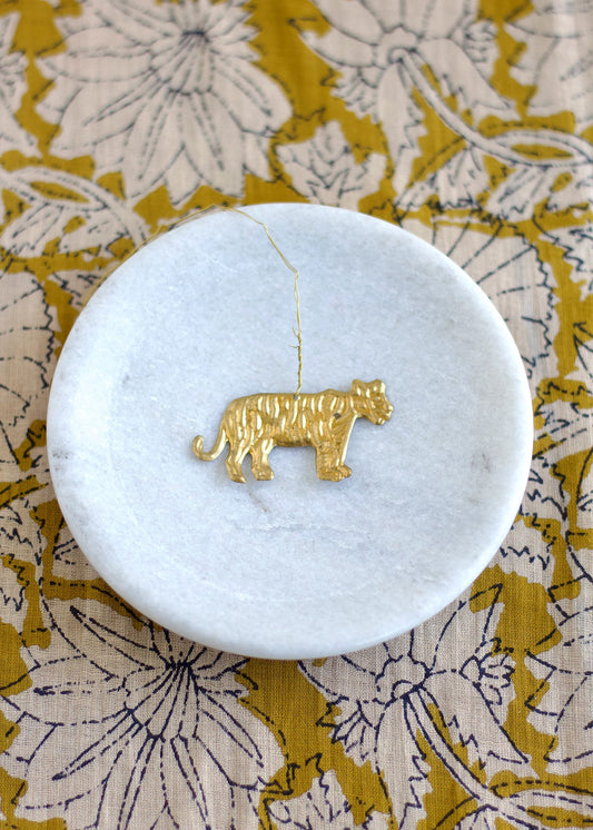 Gold tiger pendant on a white marble coaster with a floral patterned surface