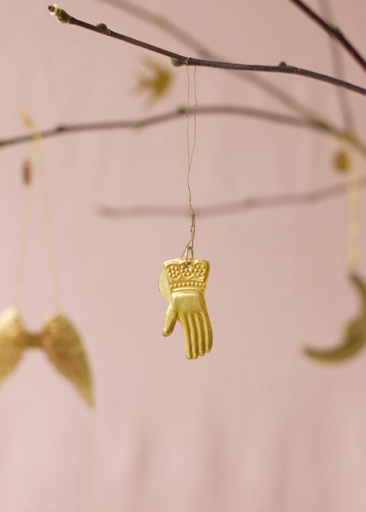 Small golden brass hand ornament with embossed details, hanging from a branch.