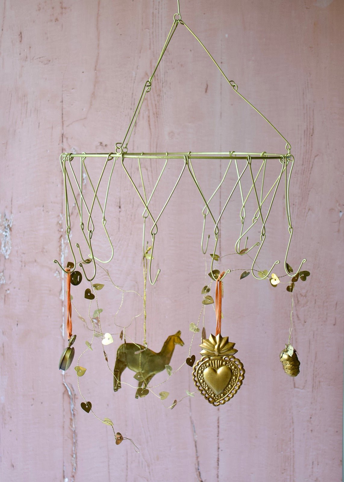 Gold-toned wire treasure hanger with hooks, adorned with hanging brass heart, horse, and decorative charms, displayed against a pale pink wall.