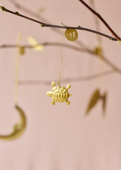 Small gold turtle ornament hanging from a branch with pink background