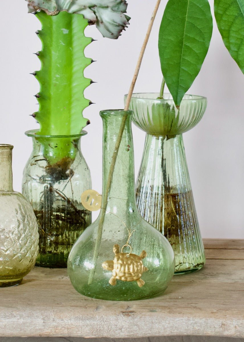 Small gold turtle ornament displayed inside a green glass vase with surrounding vintage vases