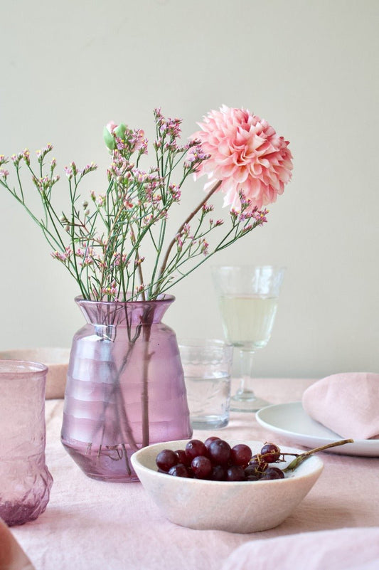 Lilac ribbed glass vase with a flared rim, filled with pink and white flowers on a softly styled table setting.

