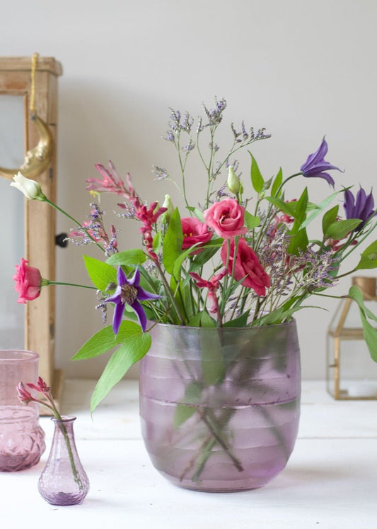 Lilac recycled glass vase with wildflowers, placed on a white surface with golden decor in the background.