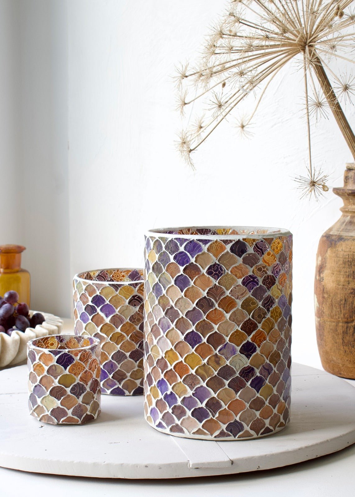 Set of three handmade mosaic glass vases in warm purple, ochre, and terracotta tones, styled in natural daylight on a white surface.