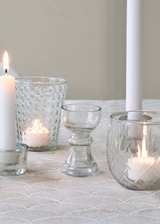 Small clear handmade glass vase with sculpted waist and rounded shape, styled on a table with candles and soft lighting.