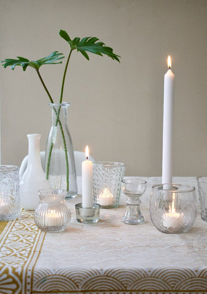 Small handmade clear glass vase with sculpted waist, styled on a dinner table with candles, other vases and green foliage.