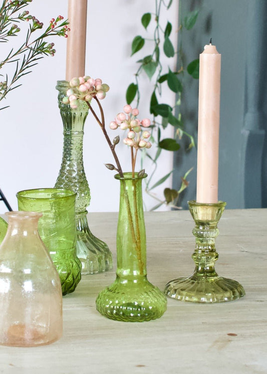 Slim green glass vase with a softly flared base and narrow neck, styled with pink berries on a wooden table.