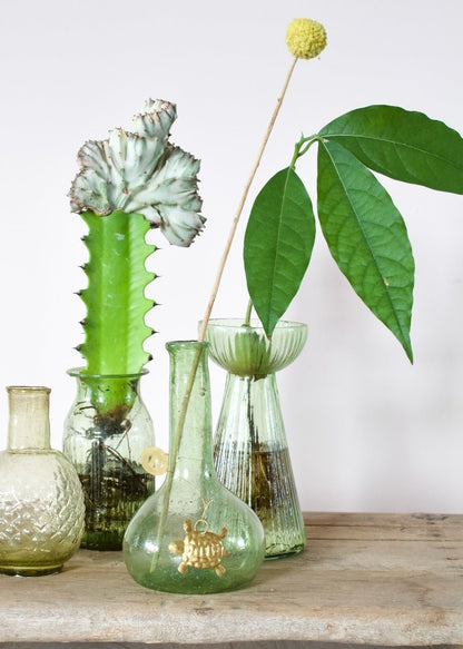 Small round recycled glass vase with short neck and a light green tint, featuring a golden turtle ornament hanging from the neck.
