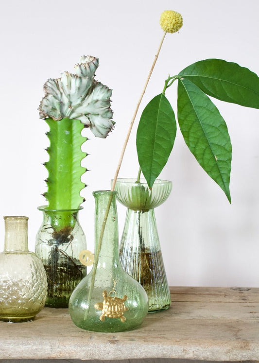 Small round recycled glass vase with short neck and a light green tint, featuring a golden turtle ornament hanging from the neck.