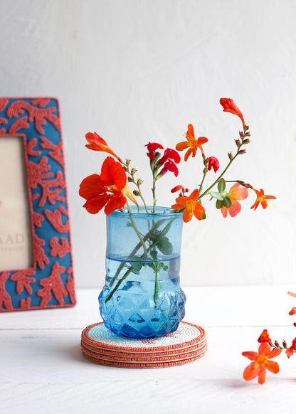 Blue textured vase with red and orange flowers on a white surface with a decorative frame in the background.