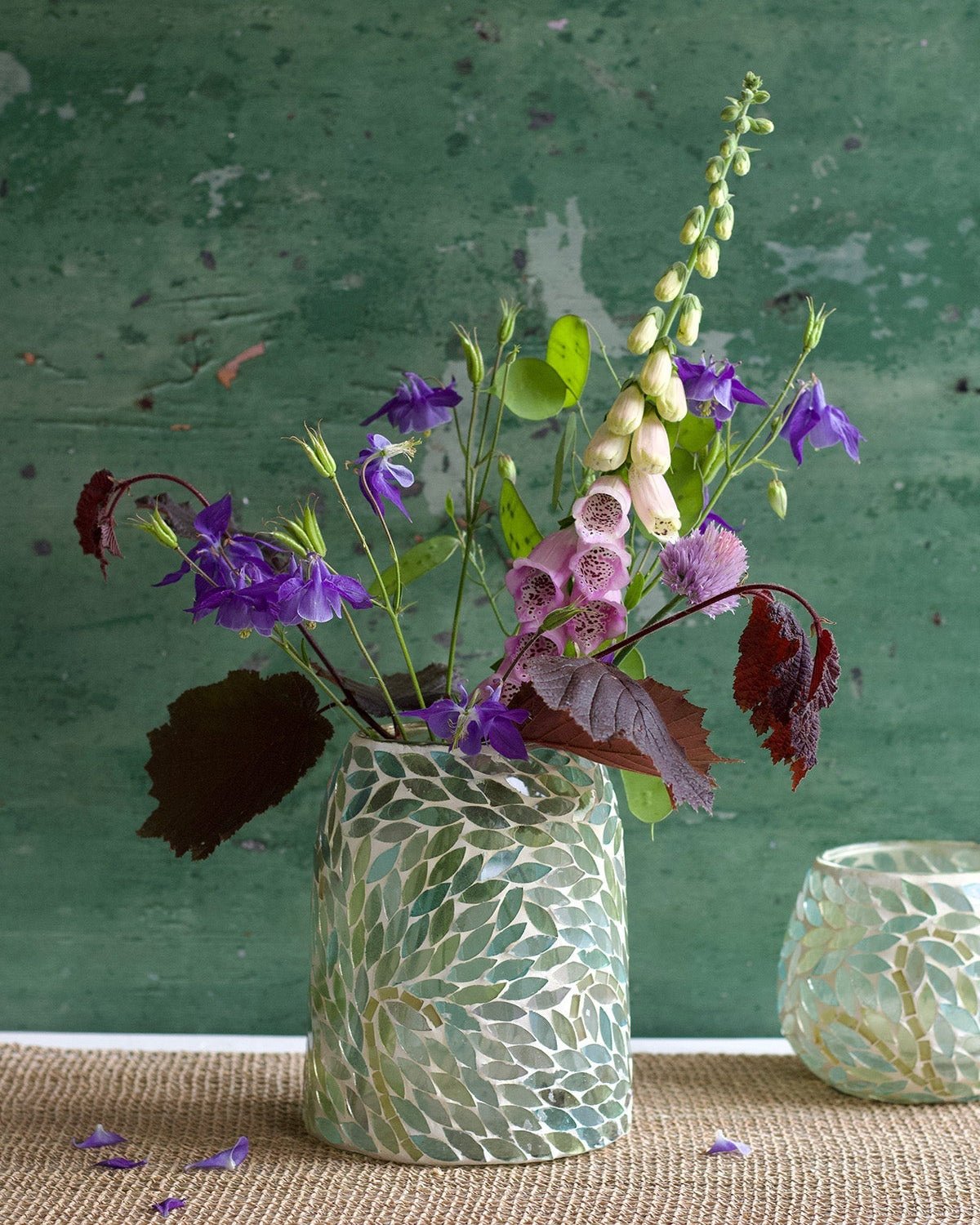 Handmade mosaic glass vase with green leaf pattern, filled with colorful wildflowers, styled against a rustic green background.