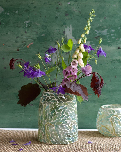Handmade mosaic glass vase with green leaf pattern, filled with colorful wildflowers, styled against a rustic green background.