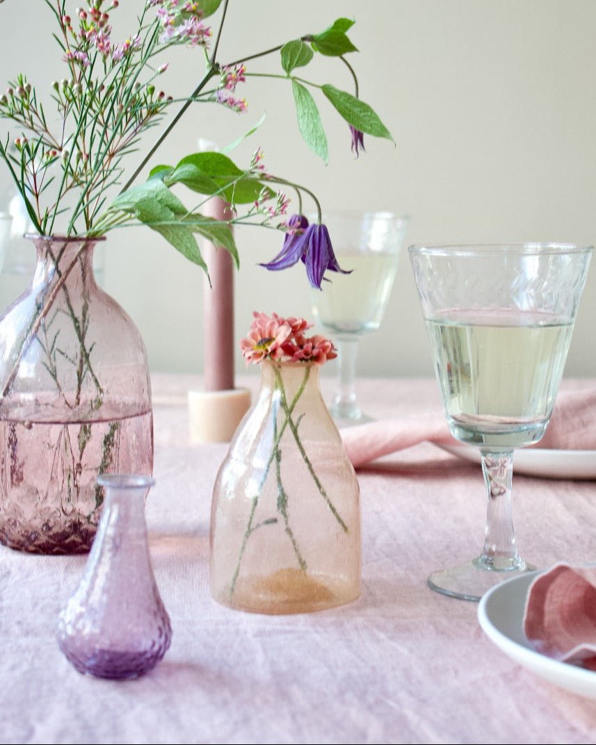 Table setting with glass vases and flowers on a pink tablecloth.