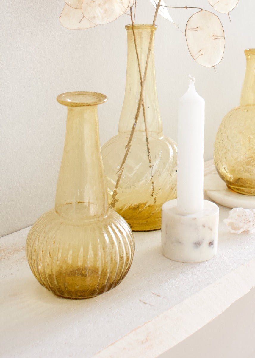 Hand-blown amber ribbed glass vase on a light wooden shelf, styled with other glass vases and a marble candle holder.