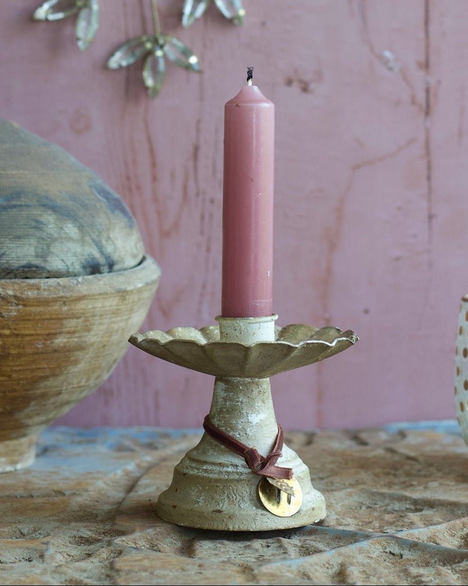 Pink candle on a decorative holder with a pink wall and hanging decorations in the background