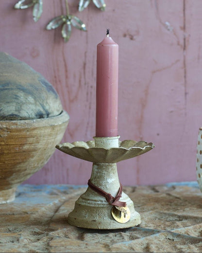 Pink candle on a decorative holder with a pink wall and hanging decorations in the background