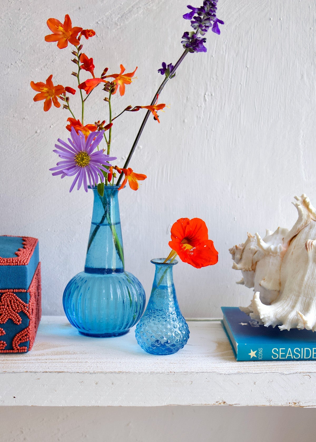 Two blue vases with colorful flowers on a white surface with a white background