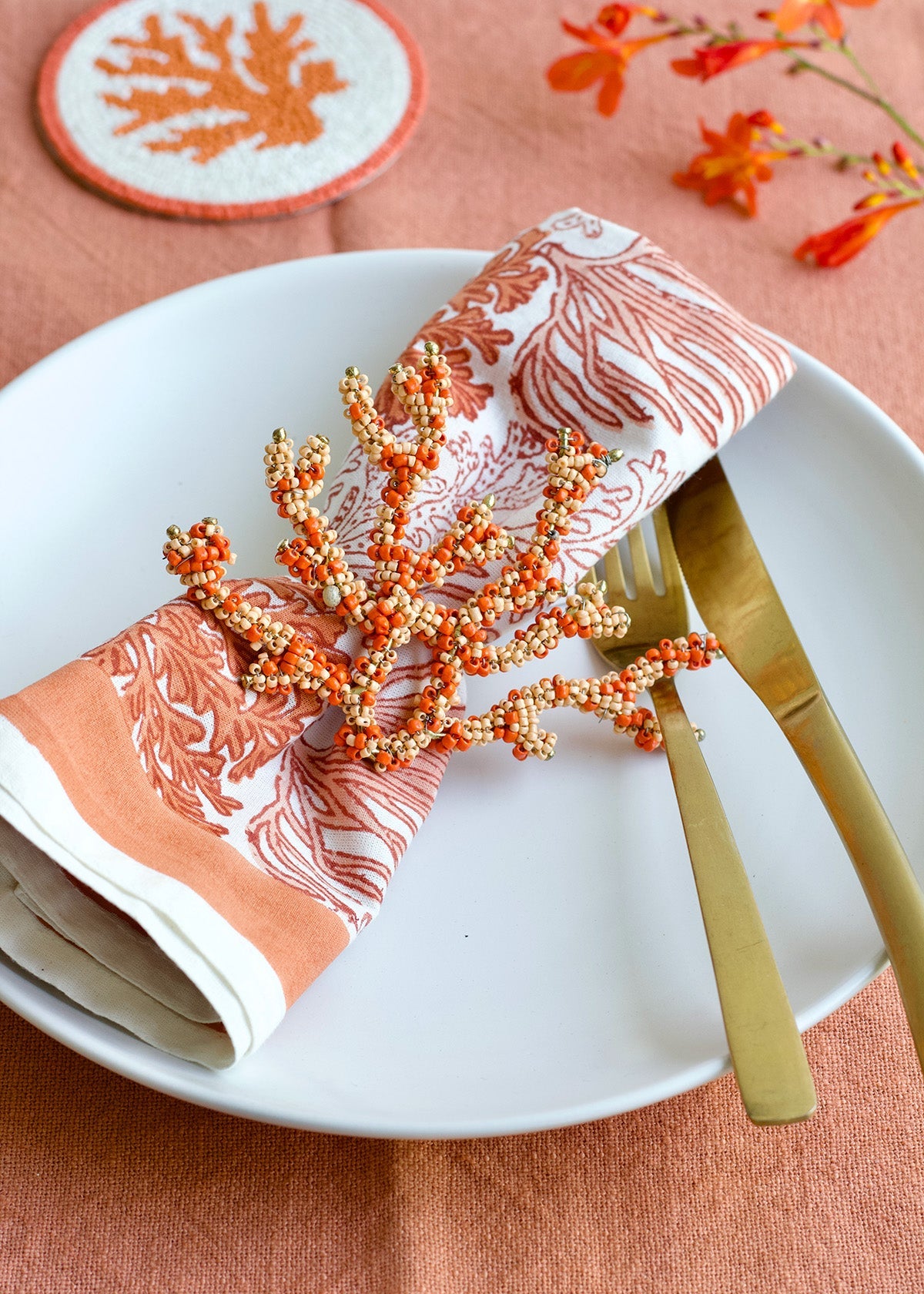 Decorative table setting with coral-themed napkin, beads, and cutlery on a white plate.