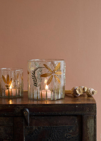 Decorative candle holders with floral designs on a wooden surface against a pink wall.