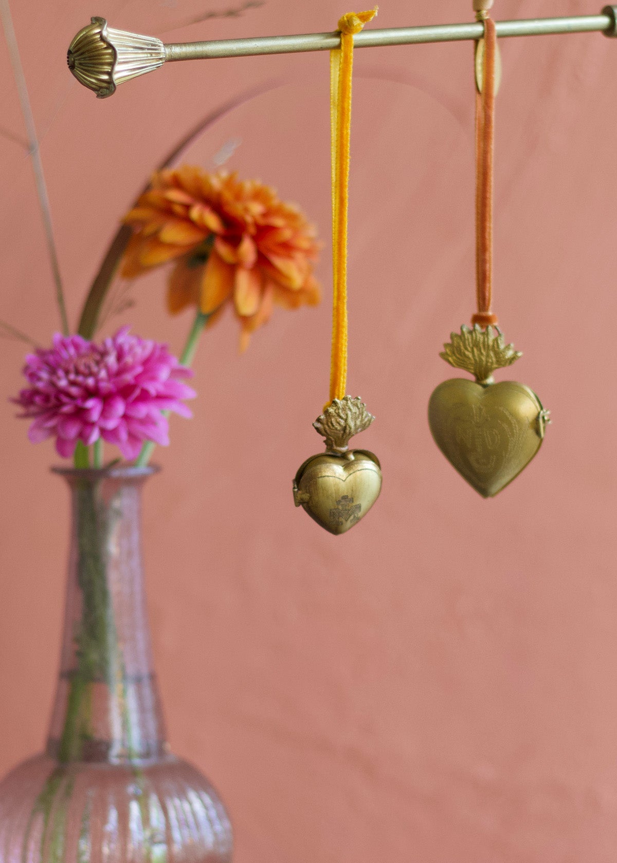 Brass heart-shaped ornaments hanging from a rod with a pink background
