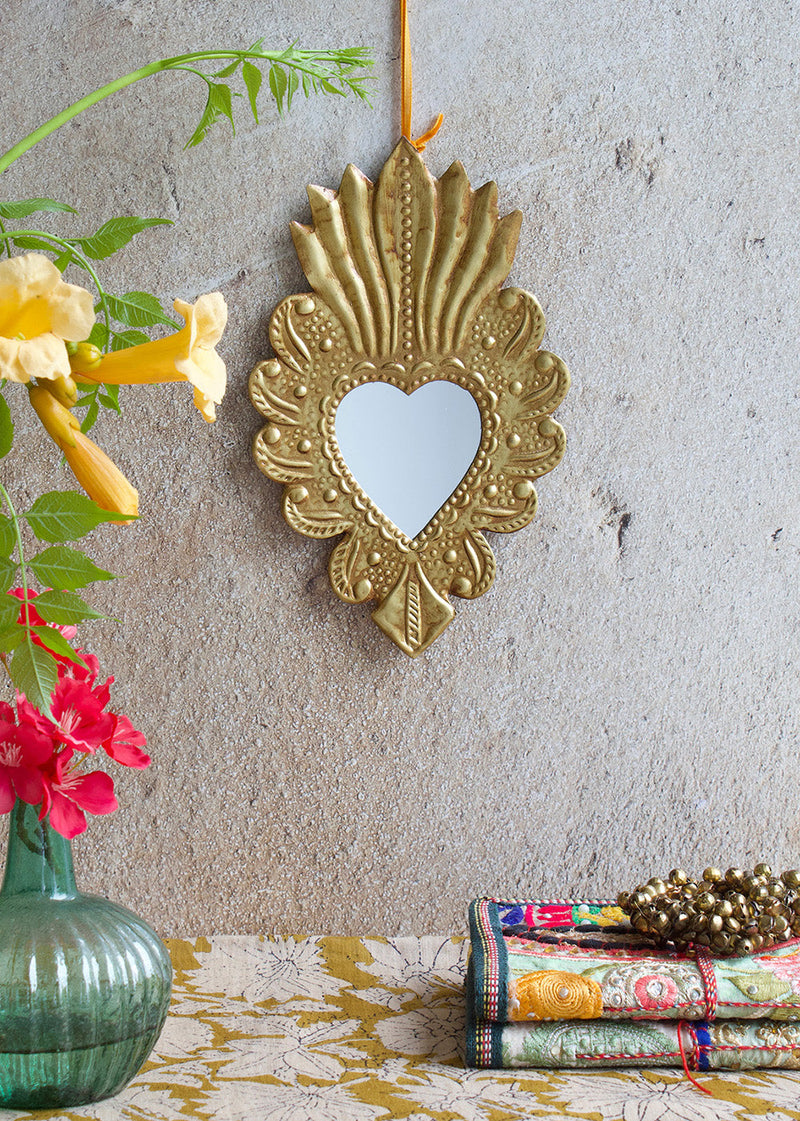 Decorative gold heart-shaped mirror on a textured wall with flowers and fabric in the foreground.