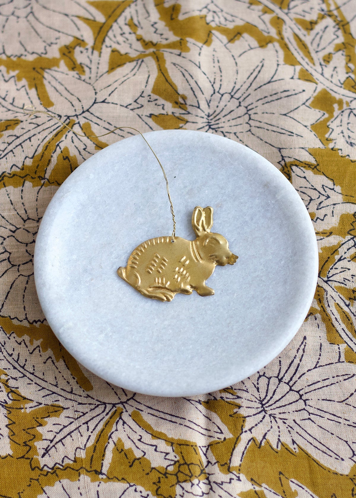 Gold rabbit-shaped pendant on a white dish with a floral patterned background