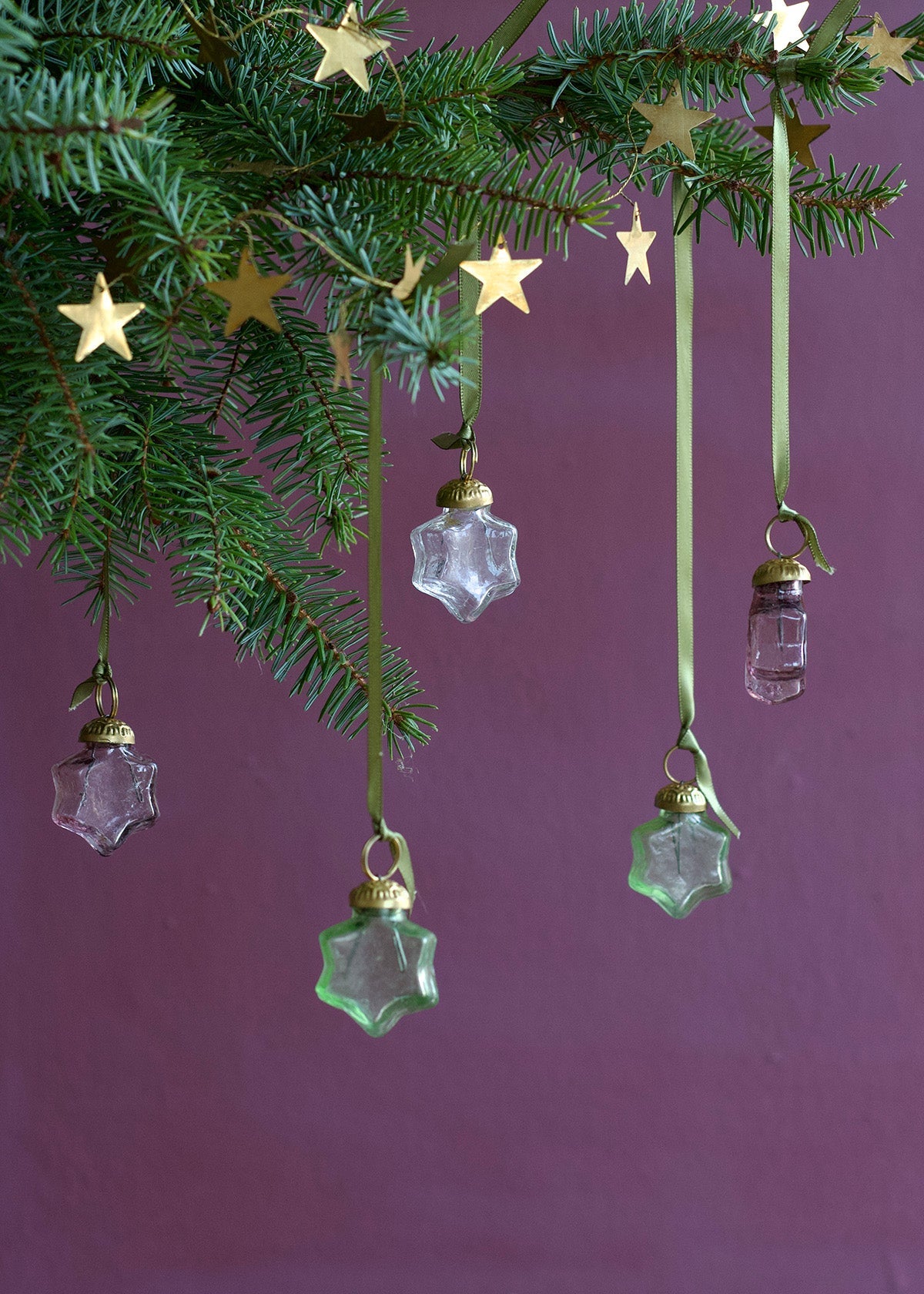 Decorative Christmas ornaments hanging from a tree with a purple background