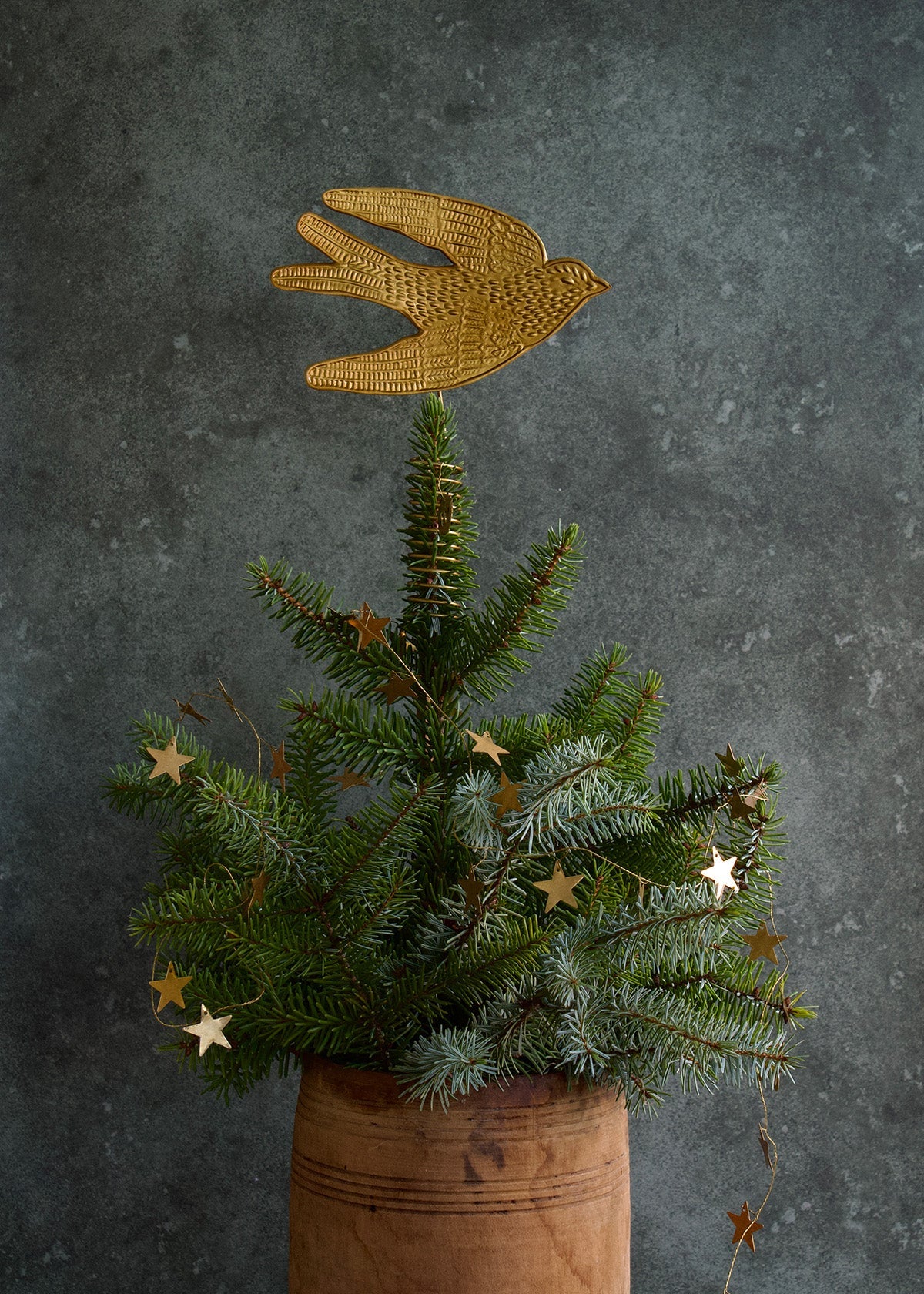 Decorative gold bird on top of a small Christmas tree with stars against a dark background