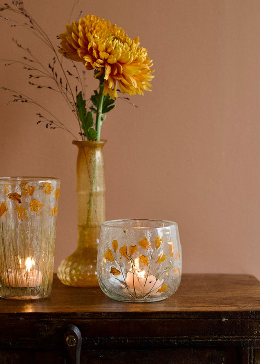 Decorative glass candle holders with floral patterns on a wooden surface against a beige wall.