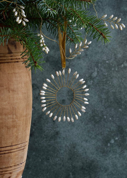 Decorative ornament hanging from a branch with a textured vase and dark background