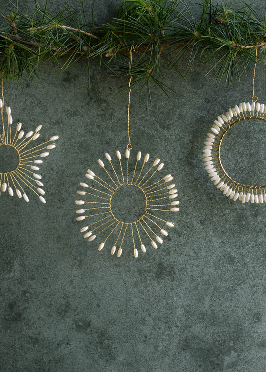 Decorative circular ornaments with white beads on a textured green surface with pine branches.