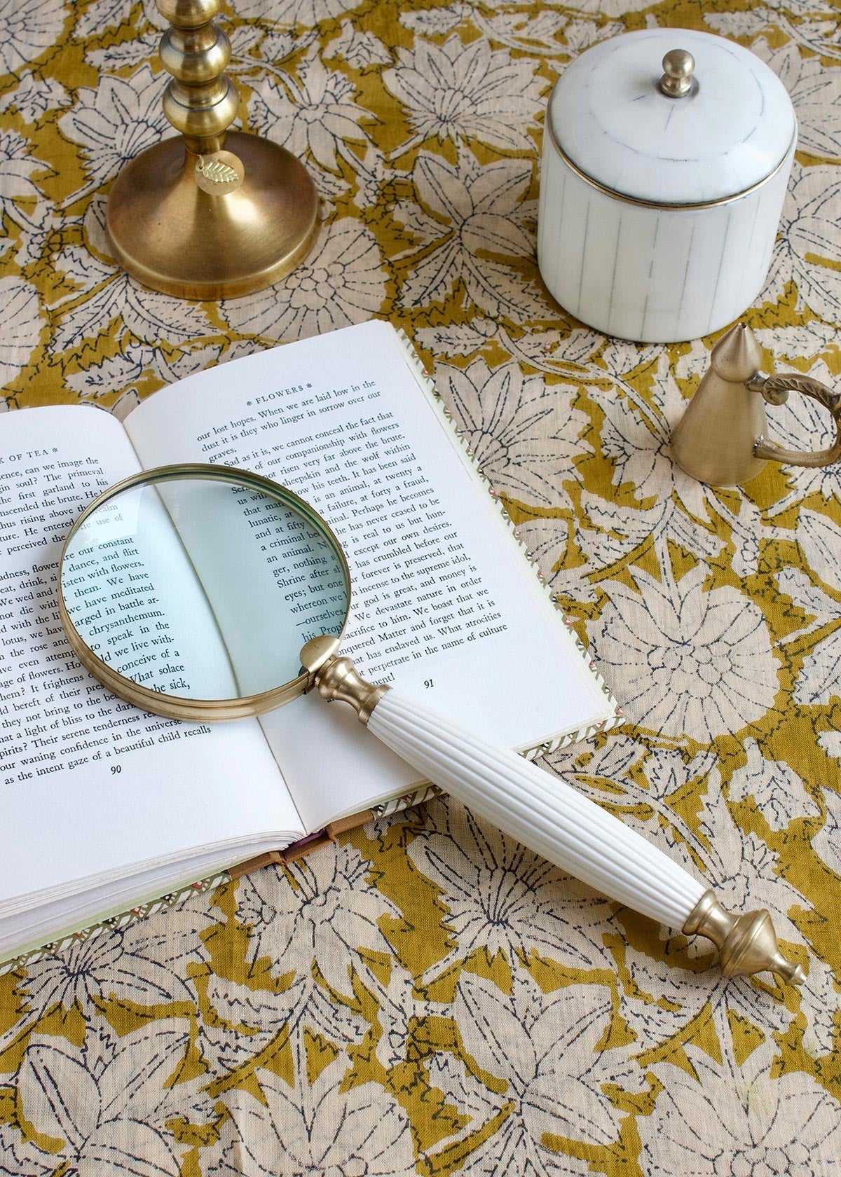Open book with a magnifying glass on a floral-patterned surface