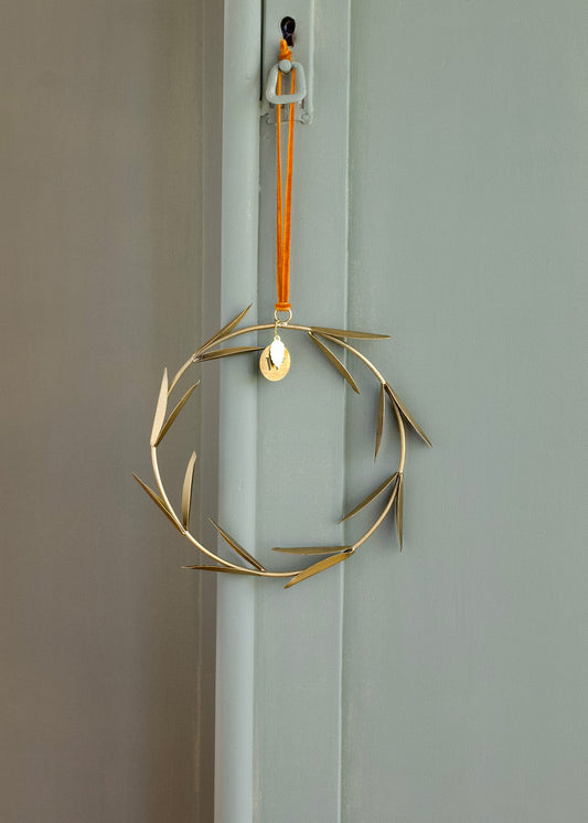Decorative gold wreath with a orange velvet string hanging on a door